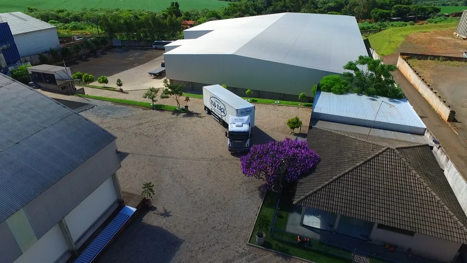 Vista aérea da fábrica da Rud Rack em Rolândia, com um caminhão da empresa no pátio e um ipê-roxo florido